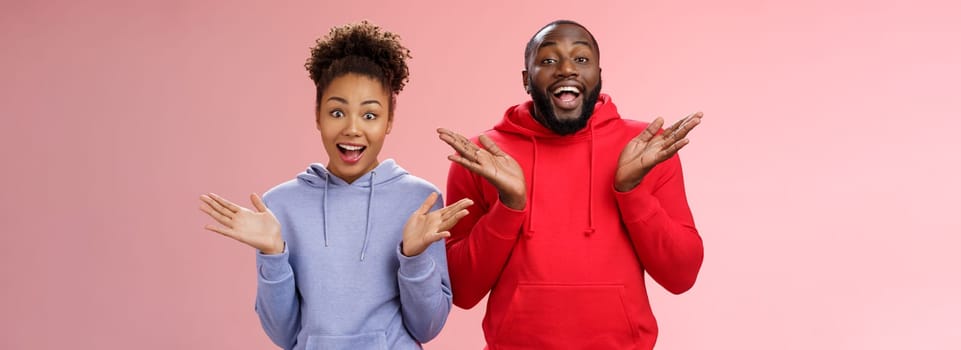 Impressed happy thrilled young pair african man woman relationship clapping palms joyfully surprised wide eyes joyfully greeting friends inviting come in hospitable, standing pink background.