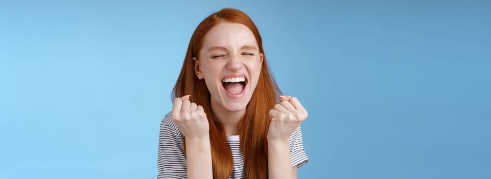 Yes achievement goal lifetime. Smiling happy european redhead girl raising clenched fists cheerful rejoicing yelling yeah accomplish goal success triumphing victory, great news win lottery.