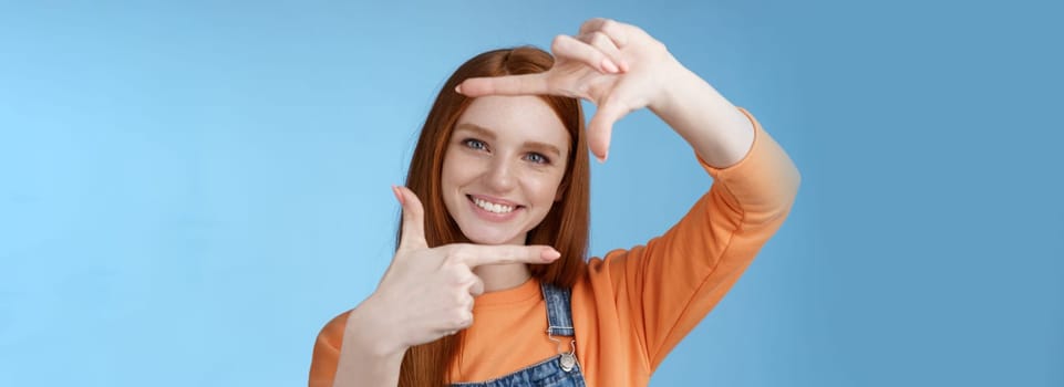 Creative good-looking nice redhead female assistant searching inspiration make hand frame look through delighted smiling satisfied found great spot take shot standing blue background.