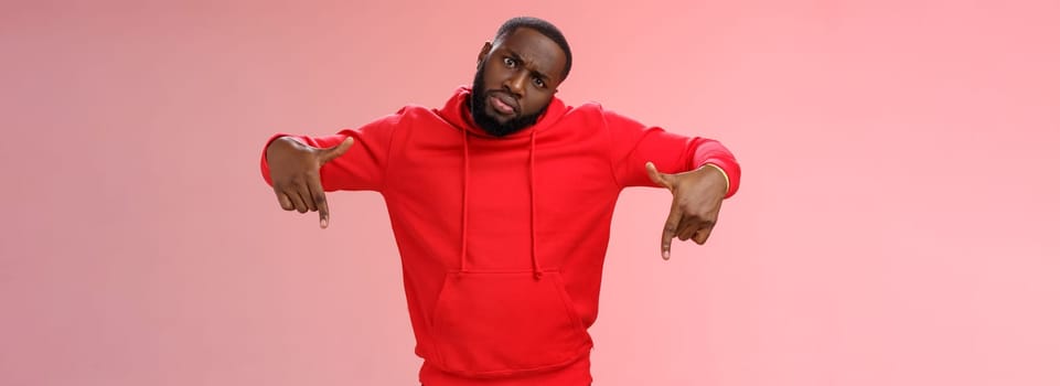 Cheeky stylish good-looking black bearded guy look cool tilting head bossy confident frowning seriously pointing down showing awesome place hang out homies, standing pink background.