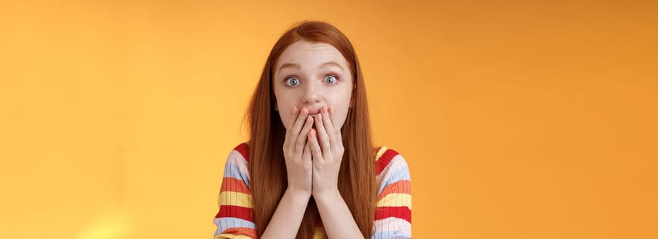 Excited shocked redhead speechless girl like gossiping standing emotional astonished hear amusing story gasping full disbelief cover mouth palm amazed posing orange background impressed.