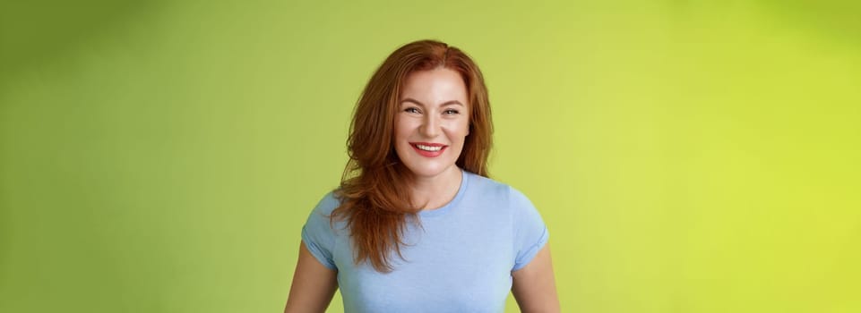 Cheerful kind happy redhead middle-aged mother look caring delighted smiling broadly gaze admiration joy stand blue t-shirt green background amused enthusiastic expression. Copy space