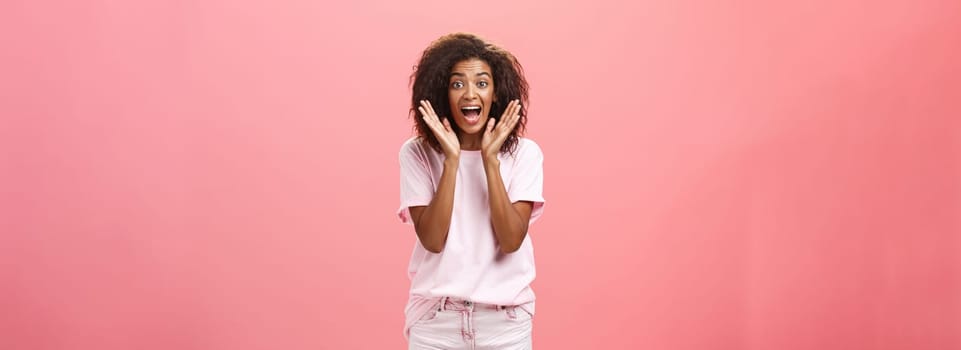 Indoor shot of expressive excited attractive dark-skinned adult woman in casual outfit yelling from amazement and joy holding palms near face reacting on awesome news with excitement and happiness. Lifestyle.