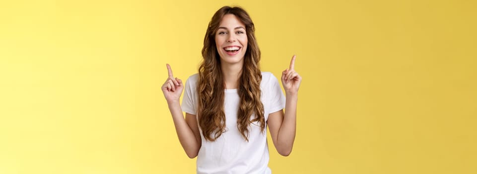 Charismatic enthusiastic attractive lively woman having fun enjoy awesome night out party laughing joyfully pointing up index fingers up introduce promo smiling happily yellow background.