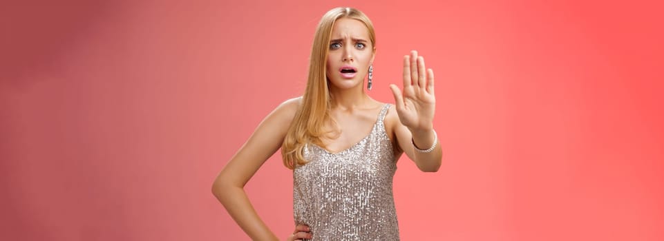 Freaked out displeased bothered insecure blond woman in silver glittering dress extend palm stop enough prohibition rejection gesture bothered pissed annoying clingy man nightclub, red background.