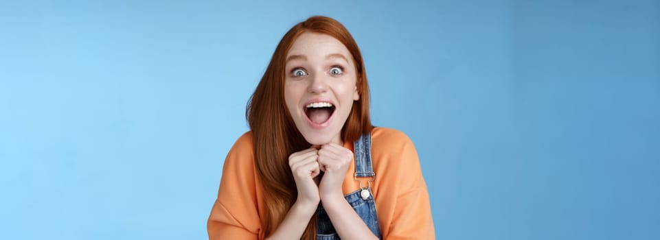 Lifestyle. Cute redhead european girl blue eyes freckles reacting amused shocking rumor lift eyebrows drop jaw surprised smiling excited picked get role theatre play rejoicing astonished blue background.