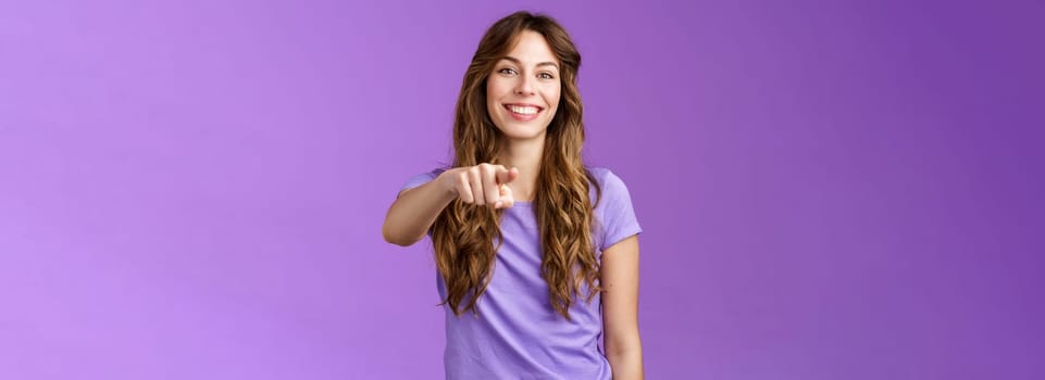Cheerful girl pointing you. Attractive friendly happy smiling curly-haired female deciding who pick indicating finger camera grinning joyful inviting coworker her team stand purple background.