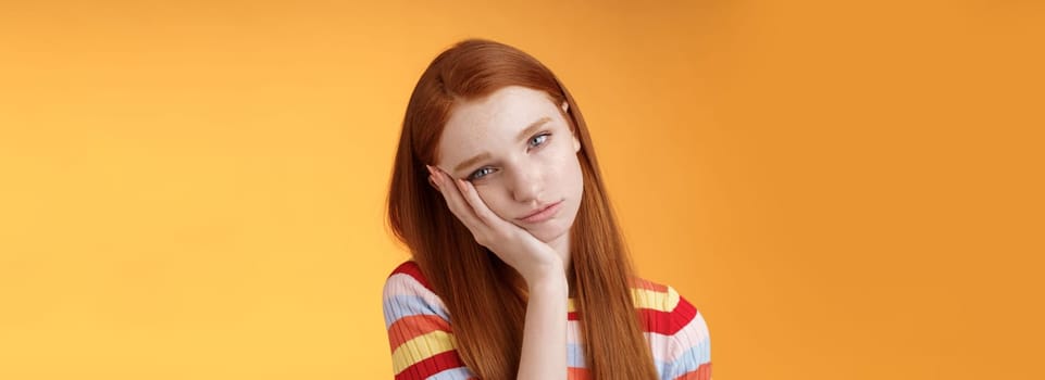 Indifferent careless sleepy redhead silly female student lean palm looking bored uninterested listen lame stories wanna escape standing exhausted lacking interest, posing orange background.