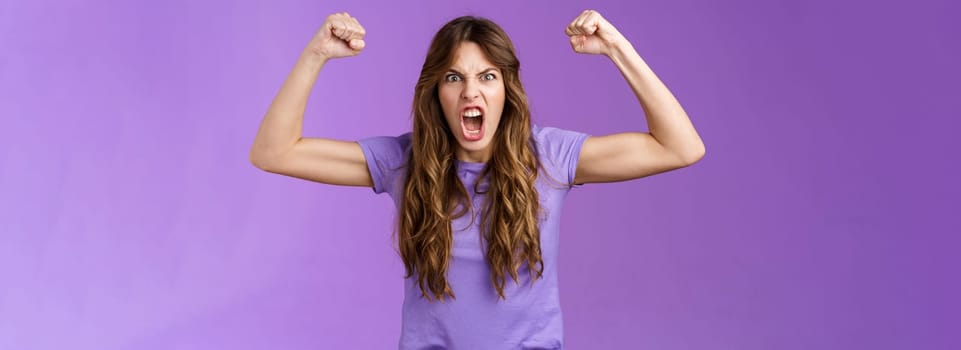 Funny curly-haired girl raising hands fist pump show muscles yelling daring cool shouting encouraged motivated win grimacing strong powerful woman celebrating victory feel like champion. Lifestyle.