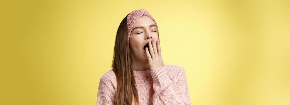 Time to bed. Portrait of tired cute sleepy girlfriend wearing sweater, knitted headband yawning cute with closed eyes opened mouth covered with palm, exhausted, wanting sleep, dreaming fall asleep.