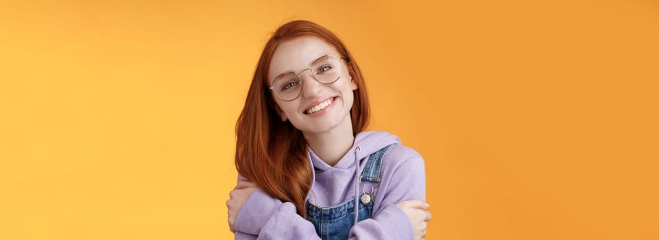 Tender romantic european redhead girlfriend tilting head cute lovely smile white teeth tilting head hugging herself wearing best friends hoodie adore new outfit grinning joyfully, orange background.