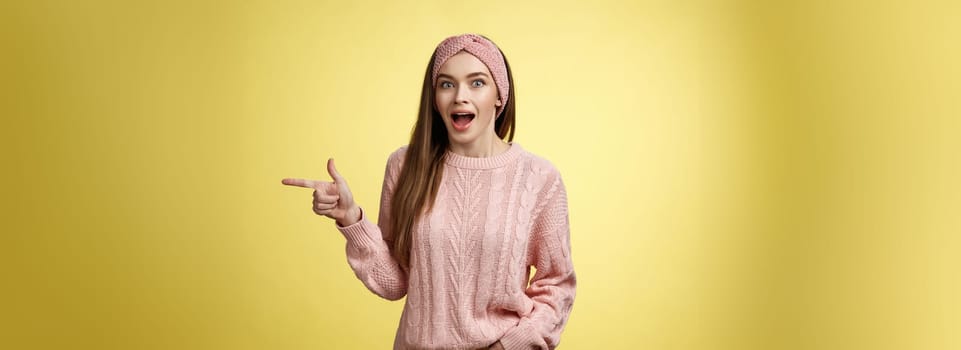 Amused thrilled attractive young female sharing amazement and excitement pointing right dropping jaw seeing unbeliavable awesome product, girl astonished advertising cool promo over yellow background.