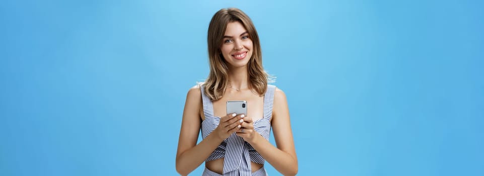 Friendly pleasant good-looking woman in matching outfit holding smartphone over chest tilting head smiling broadly showing cute gapped teeth being delighted after reading heartwarming message. Lifestyle.