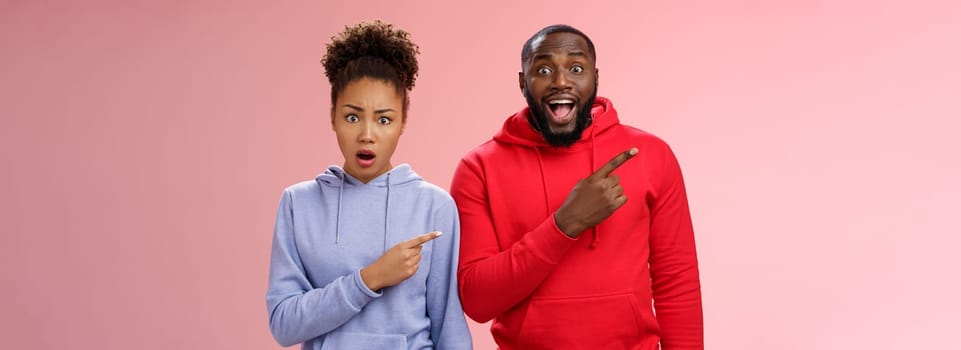 Girlfriend shocked boyfriend friends made surprise party look frustated displeased pointing upper left corner man feeling amazed thankful smiling delighted standing pink background.