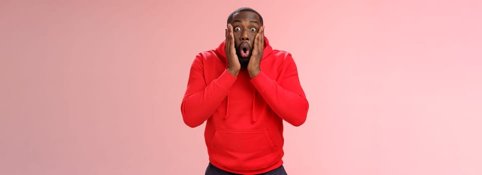 Wow incredible. Portrait impressed surprised african-american bearded guy in red hoodie folding lips bending widen eyes shocked see incredible offer standing amused excited, pink background.