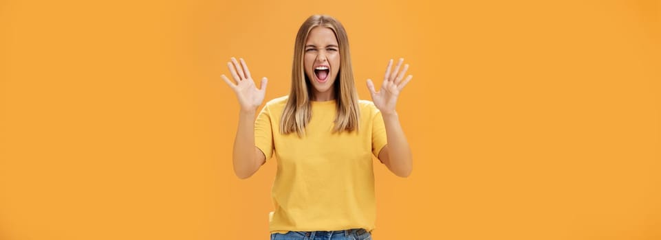 Woman releasing stress yelling with joy and pleasure gesturing with raised arms being daring and rebellious not afraid to show emotions standing passionate and expressive against orange background. Body language concept