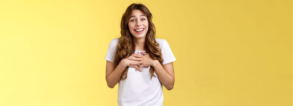 Surprised touched grateful charming caucasian curly-haired female appreciate effort thanking awesome gift press hands heart moved lovely nice present smiling broadly thankful yellow background.