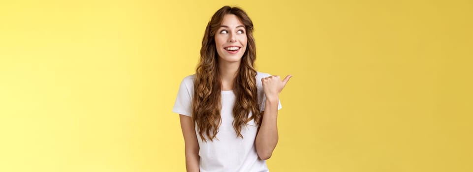 Something interesting right there. Curious lively enthusiastic charming woman glancing pointing thumb left smiling broadly discuss cool event laughing carefree stand yellow background.