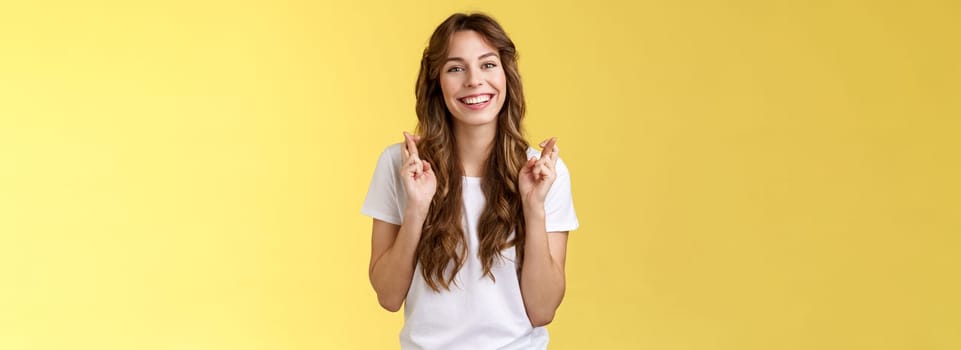 Girl faithfully believe dream come true hopefully awaiting positive results smiling broadly cross fingers good luck implore god good news stand excited optimistic yellow background.