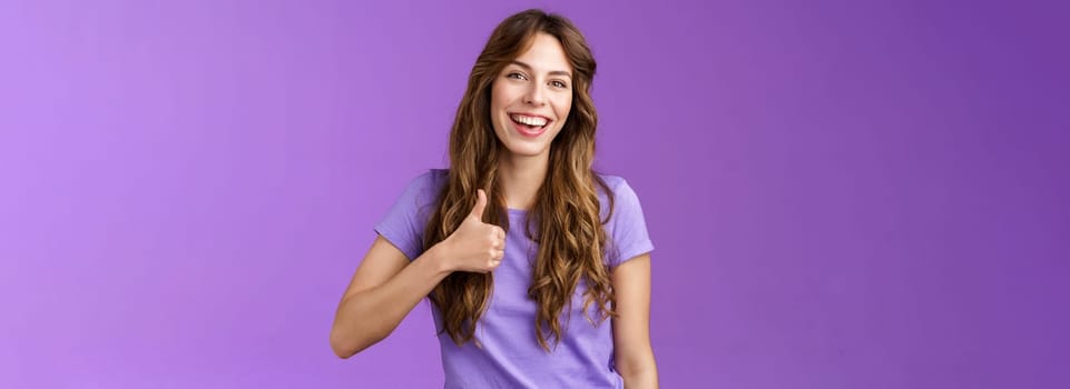 Cheerful supportive lively outgoing caucasian girl like your idea positive opinion give approval show thumbs up satisfied smiling broadly accepting great plan stand purple background.