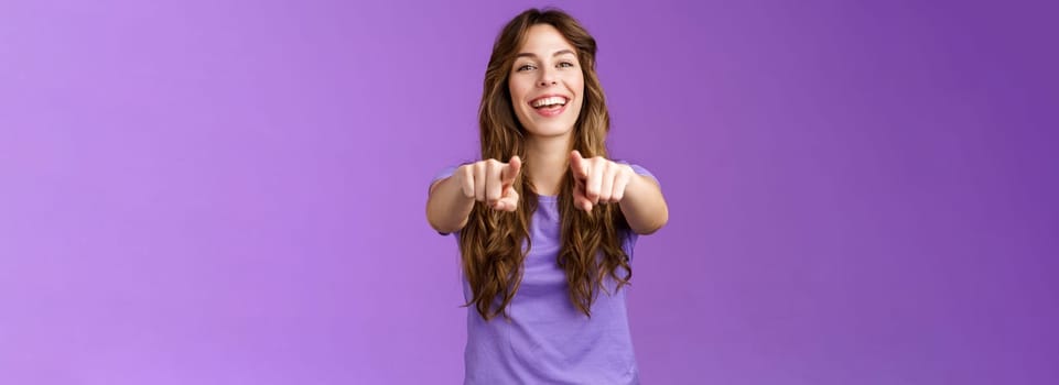 Its you. Friendly glad joyful happy curly-haired girl pointing fingers camera smiling broadly laughing congratulate friend singing song indicating boyfriend make choice stand purple background.