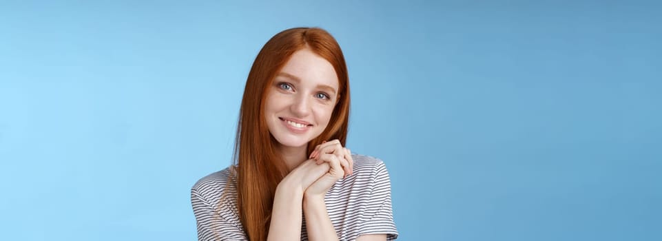 Tender romantic sincere young redhead teenage girl found love look sympathy delight press palms together cute pose smiling happily gazing camera passion lovely grin, blue background.
