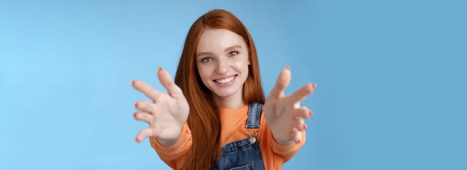 Come into arms. Charming sincere happy kind redhead girl baby sitting stretch hands camera wanna hold catch smiling friendly asking pass object, standing blue background reach friend give cuddles.