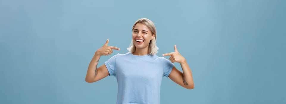 Girl proudly indicates at herself bragging with own achievements. Ambitious creative and smart attractive woman with tanned skin smiling joyfully sticking out tongue and winking pointing at chest.