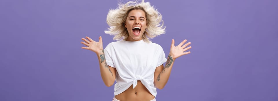 Lifestyle. Studio shot of happy carefree and pleased joyful woman with blonde hair spreading palms aside in delighted pose smiling broadly and gazing entertained at camera jumping while having fun.