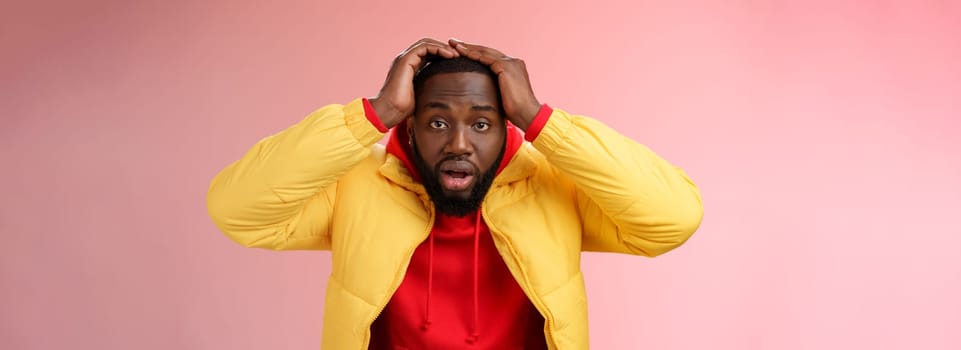 Shocked stupefied young african-american bearded man grab head drop jaw gasping confused frustrated looking upset troubled have problems standing stunned concerned pink background.
