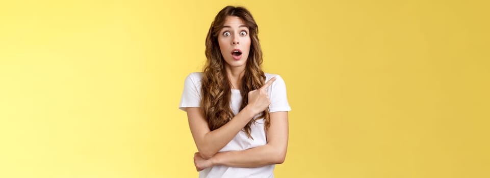 Excited impresseed speechleess shocked girl loose speech drop jaw gasping astonished asking friend advice how react stare camera opened mouth pointing left stand yellow background ambushed. Lifestyle.