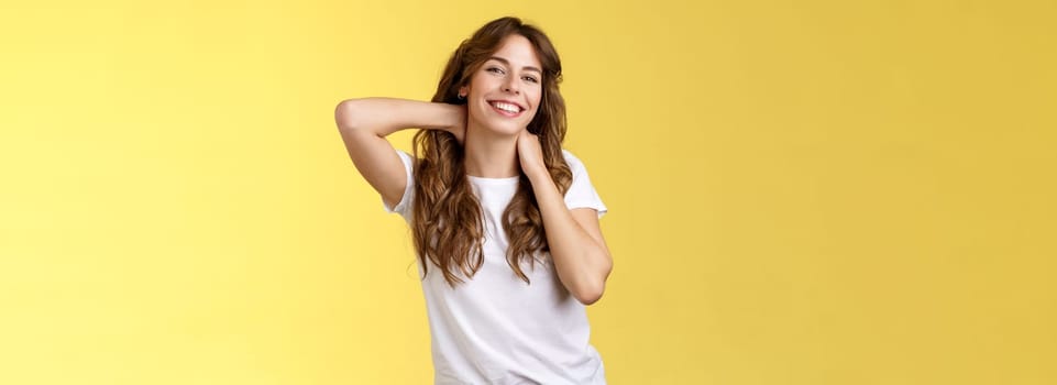 Cheerful charismatic good-looking curly-haired woman stretching posing yellow background touch neck flirty smiling relaxing perfect summer vacation booking weekend trip finally rest under sun. Lifestyle.