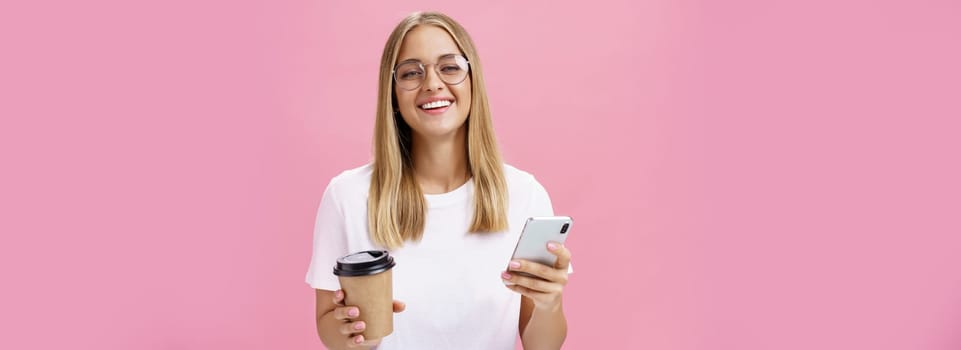 Busy freelancer sipping coffee and working via smartphone talking to clients while sitting in cafe or coworking place, laughing joyfully at camera with broad smile holding paper cup and cellphone. Van life, lifestyle, technology and digital nomad concept