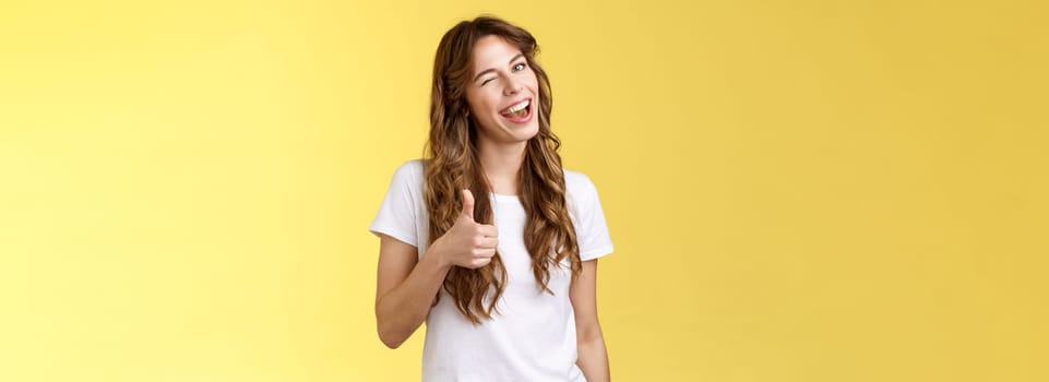 Nice well done mate. Cheerful outgoing cheeky attractive curly-haired female wink smiling nod approval show thumbs up like your choice good job accept terms stand yellow background.