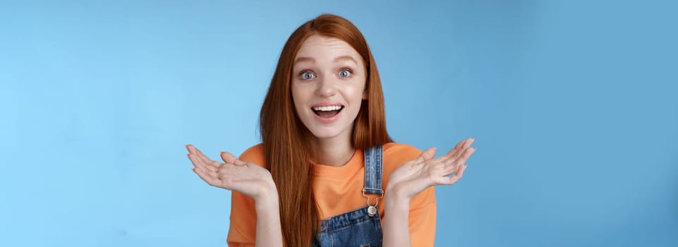 Lifestyle. Amused surprised glad young redhead girl speechless happy see friend came back hometown wide eyes impressed grinning raise hands sideways full disbelief standing blue background joyful.