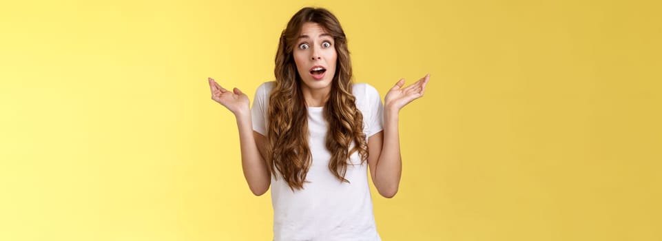 I not know. Clueless confused cute nervous young woman shrugging hands raised sideways full disbelief questioned expression lift eyebrows puzzled unable answer question stand yellow background.