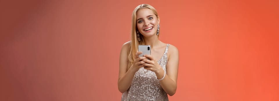Lifestyle. Charming elegant young 25s woman in silver dress brilliant accessorize holding smartphone messaging using app order taxi after nightclub friends party standing carefree smiling camera joyfully.