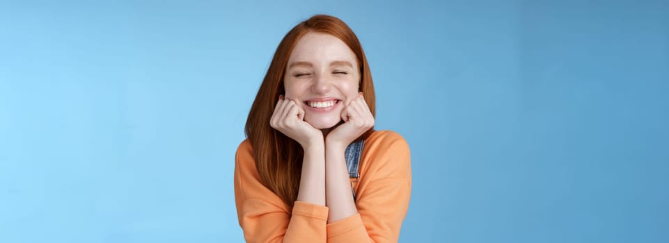 Lifestyle. Silly cute happy redhead girlfriend smiling broadly close eyes dreamy squeez cheeks delighted asked date guy likes standing blue background rejoicing have fantastic lucky day triumphing.
