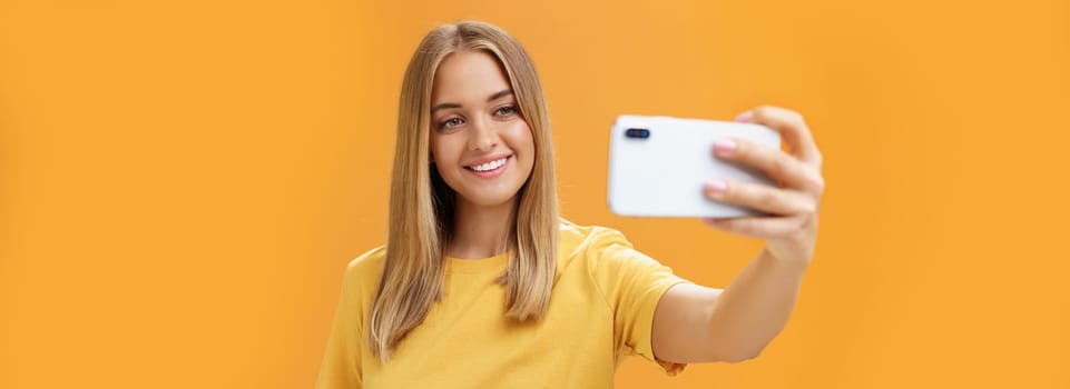 Waist-up shto of outgoing and charismatic pretty confident woman with no makeup and tanned skin holding smartphone pulled on distance smiling broadly at cellphone screen while taking selfie. Technology concept