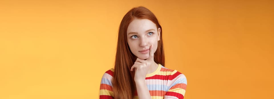 Creative thoughtful young smart redhead female student thinking ideas project look upper left corner dreamy touching lip pondering choice, taking important decision what order, orange background.