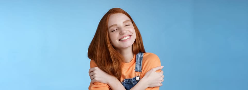 Lifestyle. Close-up dreamy happy smiling redhead girl close eyes fantasizing romantic date grinning white teeth cuddle herself cross arms chest embracing recalling lovely memories hugging daydreaming.