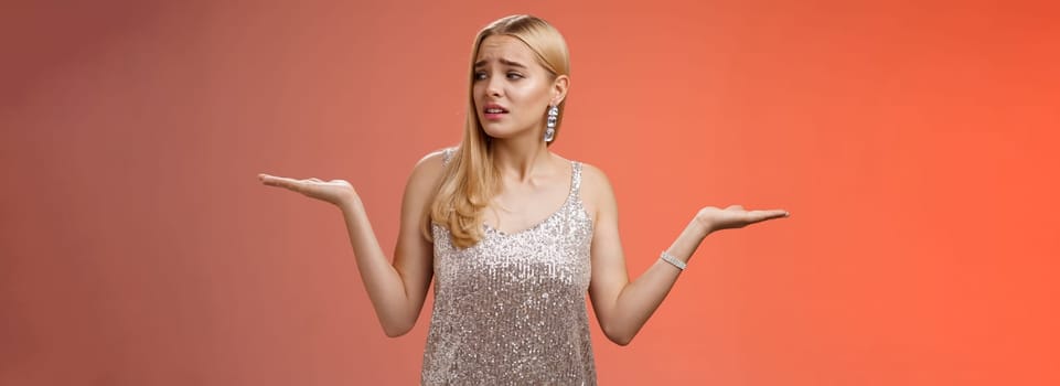 Lifestyle. Anxious insecure young cute blond girl feel lost unsure shrugging hands sideways weighing decisions look right seek help standing lost nervous hesitating red background in silver glittering dress.