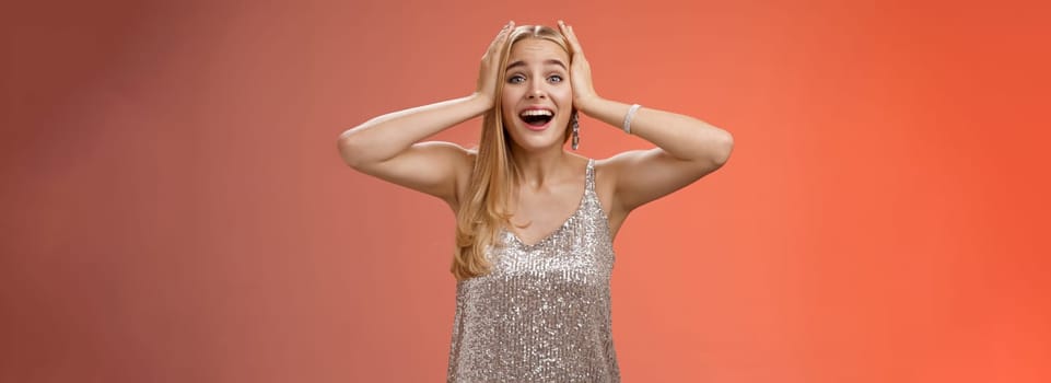 Amazed excited nervous young beautiful blond woman in silver stylish dress cannot believe own luck happiness hold hands head smiling screaming astonished positive awesome news, triumphing.