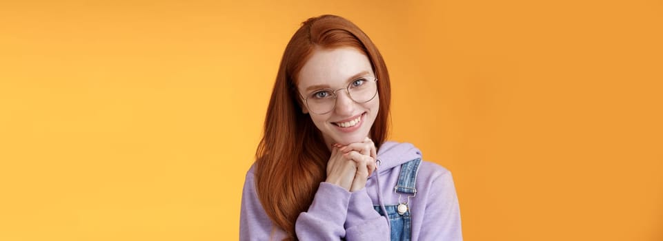 Flirty young clingy girlfriend redhead girl trying learn flirt making creepy lovely smile lean head palms seducing guy standing orange background glancing romantically wear glasses. Copy space