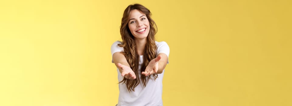 Come closer take my hand. Cheerful lovely charismatic tender woman extend arms forward camera wanna hold receive charming gift tilt head smiling pleased grateful stand yellow background. Copy space