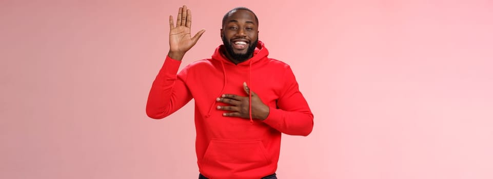 Smiling friendly african-american sincere man raise palm hold hand heart swearing loyalty pledging oath make promise standing positive pink background cheerfully grinning. Copy space