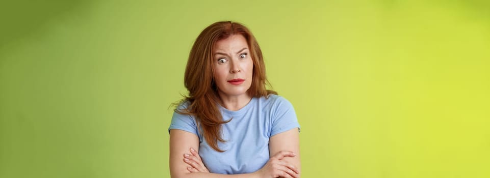 You did what. Confused shocked speechless redhead mature mother stare camera puzzled concerned cross arms chest self-soothing bothered pose look questioned hesitant green background.