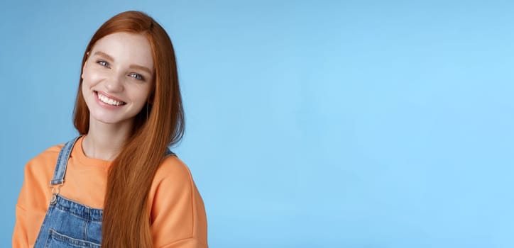 Pleasant sincere happy ginger girl blue eyes tilting head grinning happily laughing stay positive lucky spend time best friends receive praises compliments good job smiling delighted, blue background.