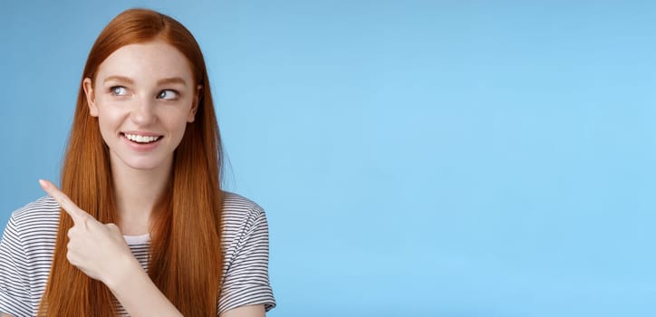 Intrigued good-looking redhead joyful curious girl watching looking upper left corner interested smiling broadly visit cool amusing place explore travelling new country astonished, blue background.