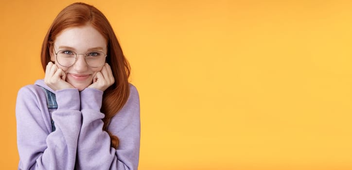 Lovely cute redhead sweet silly girl geek university student wearing glasses lean hand smiling tenderly look affection adore listen sensual confessions boyfriend, standing orange background.